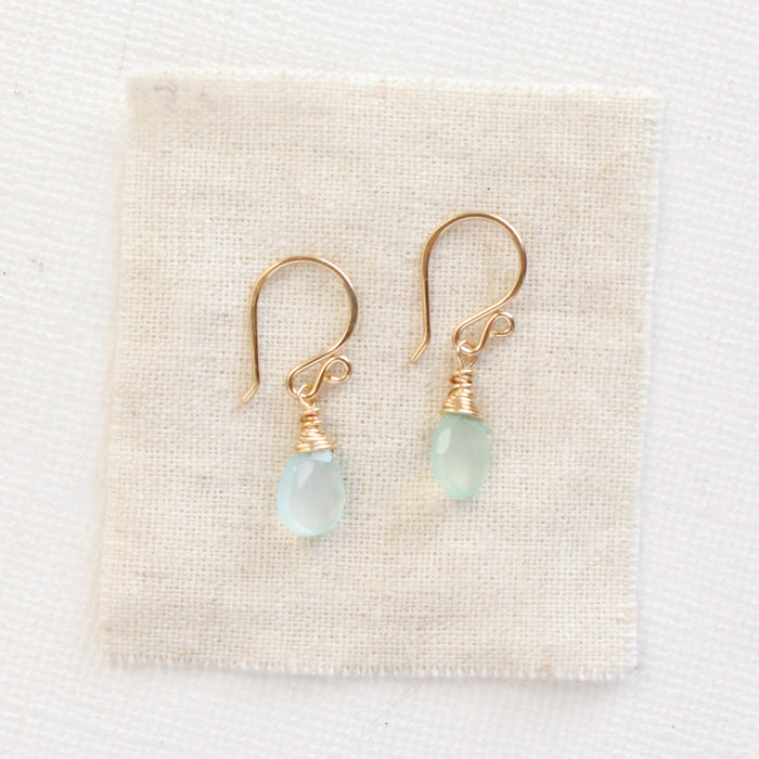 The gold chalcedony drop earrings styled on tan linen