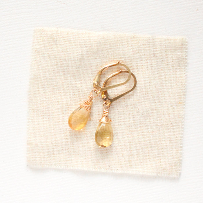 The gold citrine drop earrings styled on tan linen