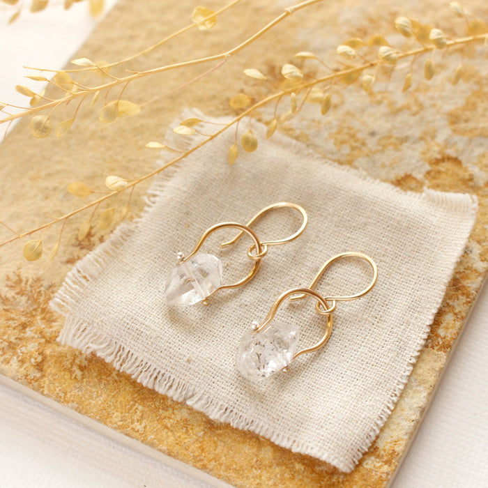 The gold herkimer diamond la cloche earrings styled on a tan rock with linen and dried grass
