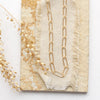 The gold paperclip necklace styled on a tan rock with linen and dried grass