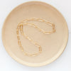 The gold paperclip necklace styled on a tan plate to show the whole chain