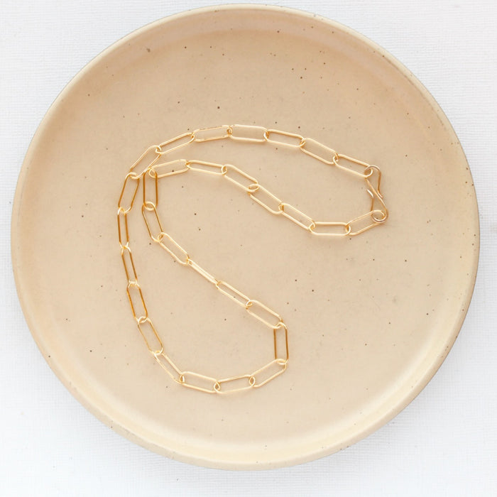 The gold paperclip necklace styled on a tan plate to show the whole chain