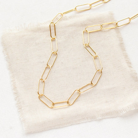 The gold paperclip necklace styled on tan linen