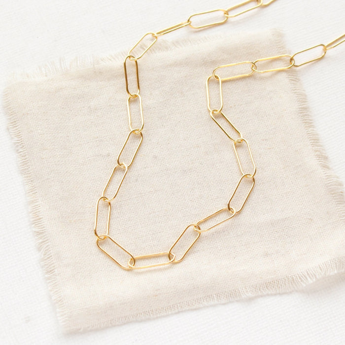 The gold paperclip necklace styled on tan linen