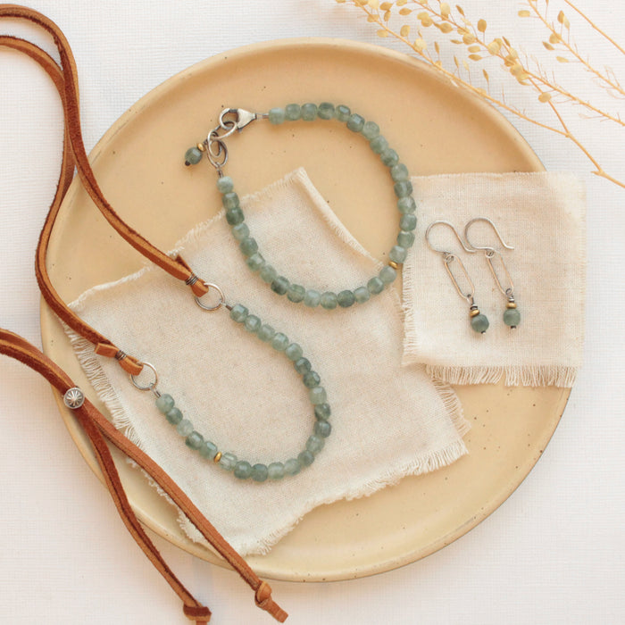 The green apatite and brass hoop earrings styled on a tan plate with the matching necklace and bracelet