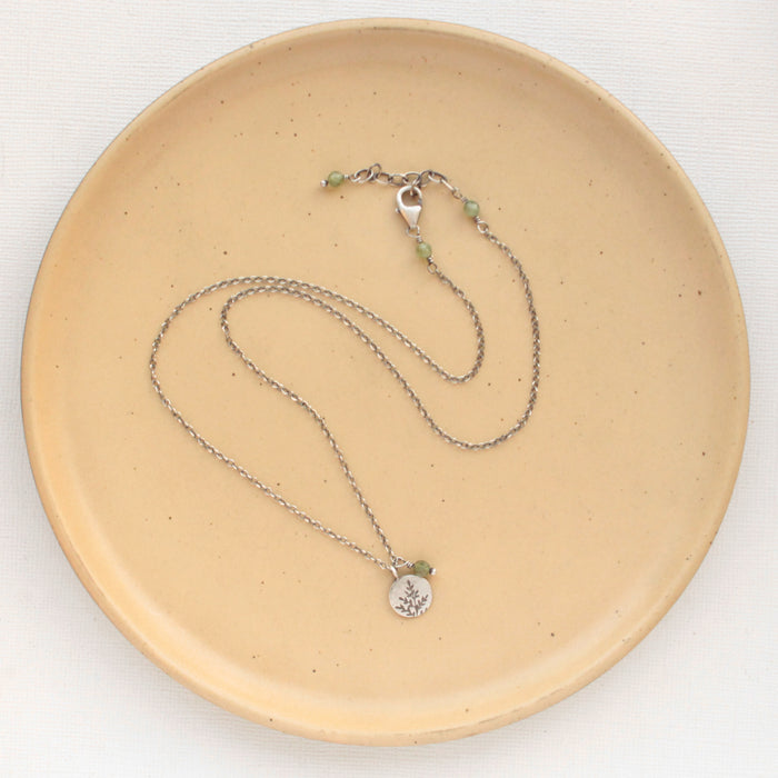The green kyanite and sprout charm necklace styled on a tan plate to show the adjustable lobster clasp closure