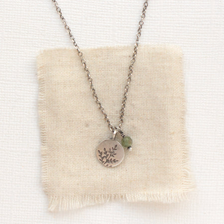 The green kyanite and sprout charm necklace styled on tan linen