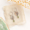 The green kyanite sprout earrings styled on tan linen with dried grass and a green rock