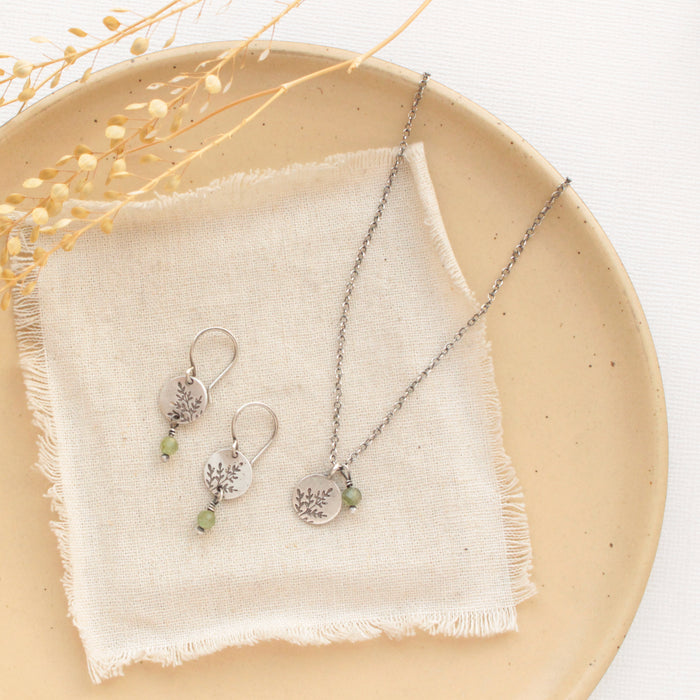 The green kyanite sprout earrings styled with the matching necklace on a tan plate with linen and dried grass