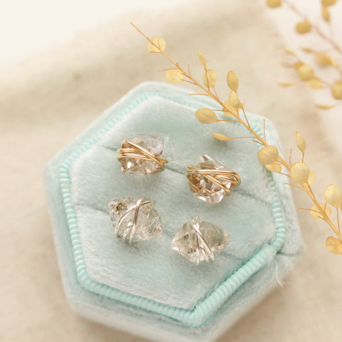 The herkimer diamond post earrings in silver and gold styled on a velvet box with linen and dried grass