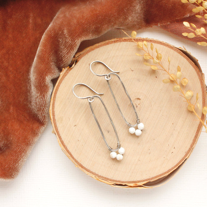 The howlite wrapped forged silver long hoop earrings styled on wood with red velvet and dried grass