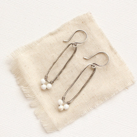 The white howlite wrapped forged silver long hoop earrings style on tan linen