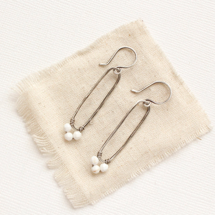 The white howlite wrapped forged silver long hoop earrings style on tan linen