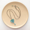 The hubei tuqurquoise heart and grandidierite necklace styled on a tan plate to show the adjustable lobster clasp closure