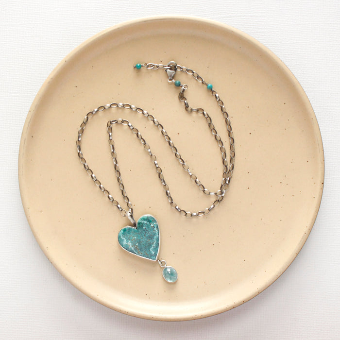 The hubei tuqurquoise heart and grandidierite necklace styled on a tan plate to show the adjustable lobster clasp closure