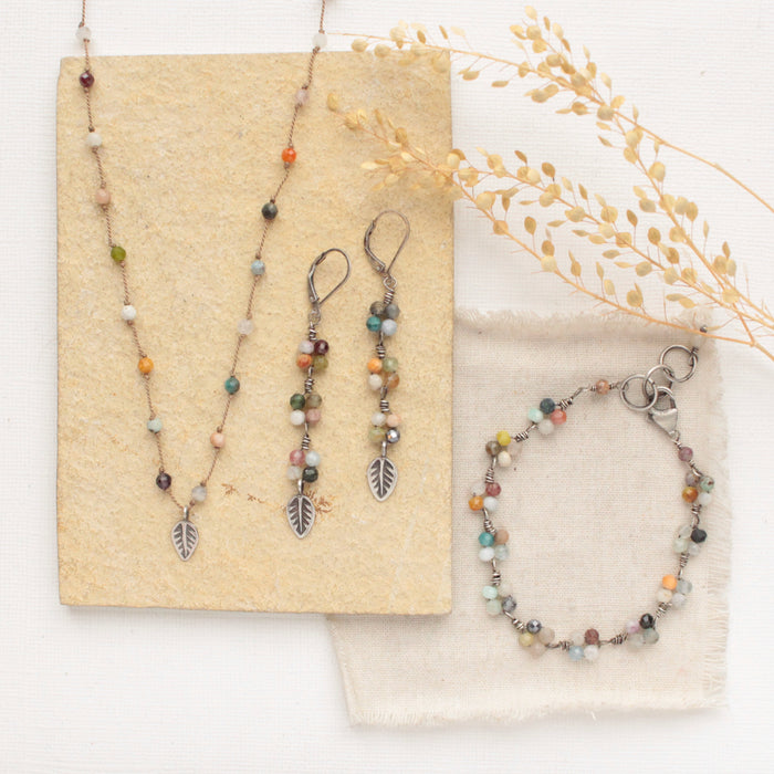 The kaleidoscope bracelet styled with the matching earrings and necklace with a tan rock, linen, and dried grass