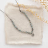The knotted zircon roma necklace styled on tan linen with dried grass