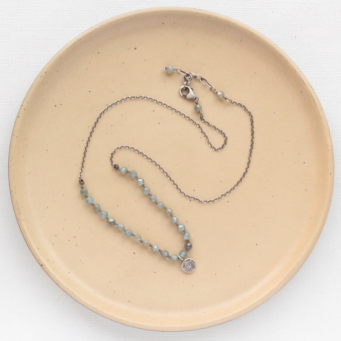 The knotted zircon roma necklace styled on a tan plate to show the adjustable lobster clasp closure