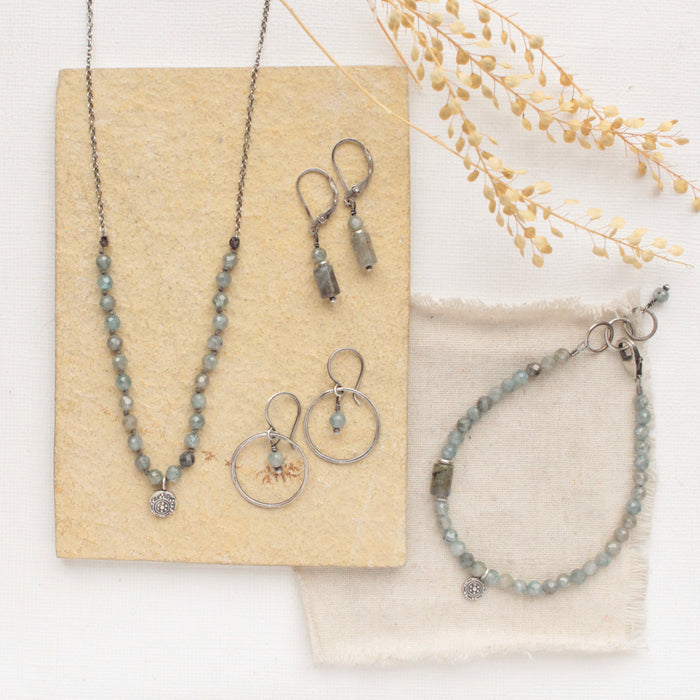 The knotted zircon roma necklace styled with the matching bracelet and two pairs of earrings on linen and a tan rock