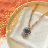 The knotted moonstone heart necklace styled on a tan plate with linen, orange velvet, and dried grass