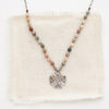 The knotted rainbow agate sun cross necklace styled on tan linen