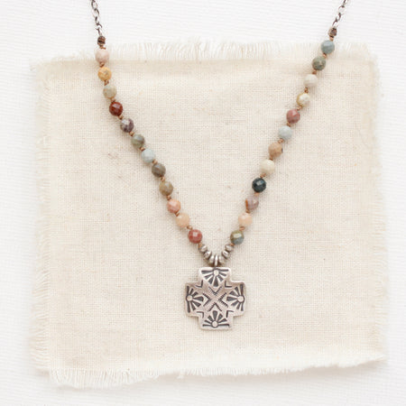 The knotted rainbow agate sun cross necklace styled on tan linen