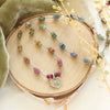 The rainbow tourmaline heart necklace styled on wood with green velvet and dried grass