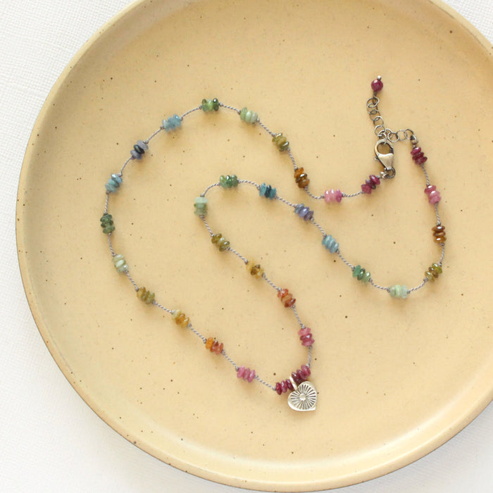 The knotted tourmaline heart necklace styled on a tan plate to show the adjustable lobster clasp closure