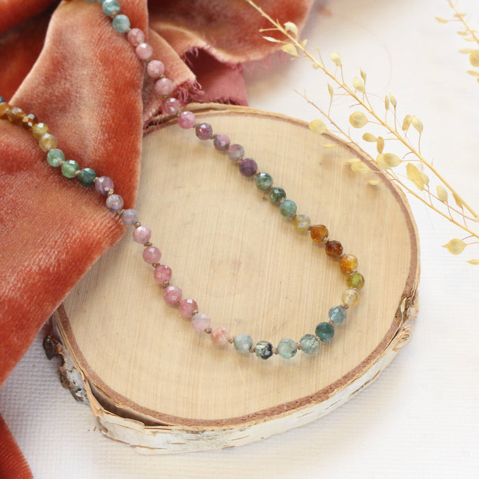 The knotted rainbow tourmaline necklace styled on wood with orange velvet and dried grass