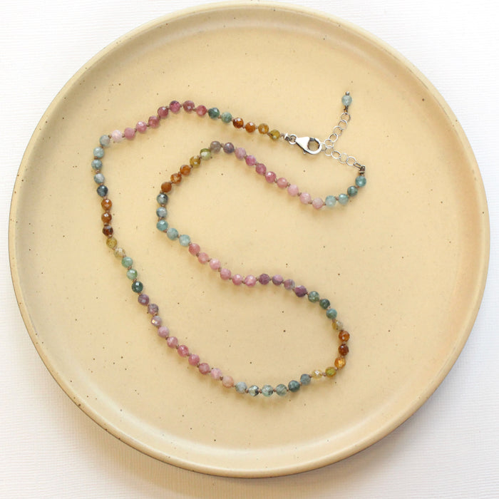 The knotted rainbow tourmaline necklace styled on a tan plate to show the adjustable lobster clasp closure