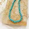 The knotted sleeping beauty turquoise necklace styled on a tan rock with linen and dried grass