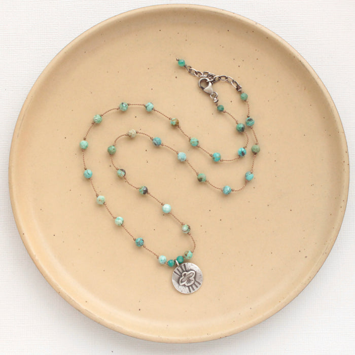 The knotted turquoise soar necklace styled on a tan plate to show the adjustable lobster clasp closure