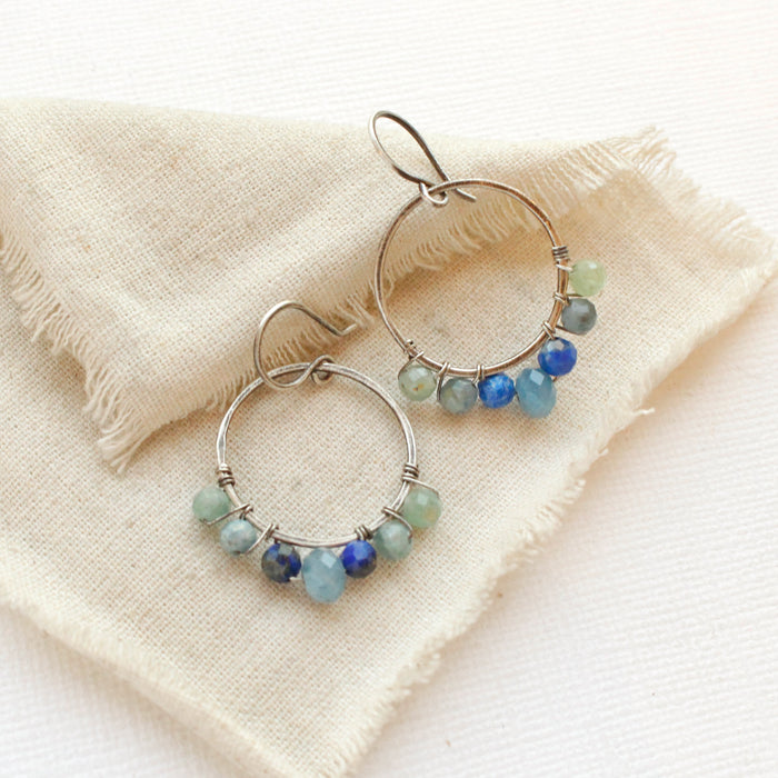 The kyanite and aquamarine hoop earrings styled on tan linen