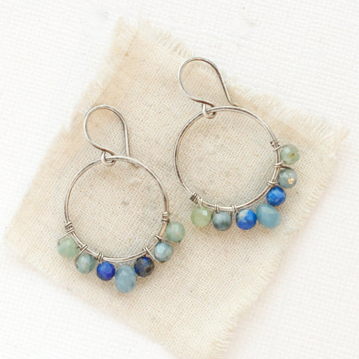 The kyanite and aquamarine hoop earrings are styled on tan linen