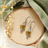 The stacked mythos earrings styled on wood with green velvet and dried grass