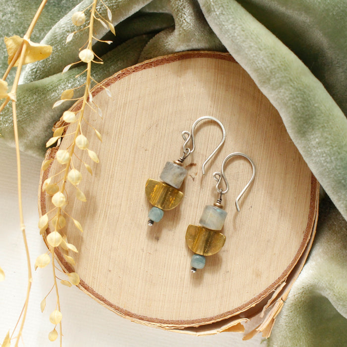 The stacked mythos earrings styled on wood with green velvet and dried grass