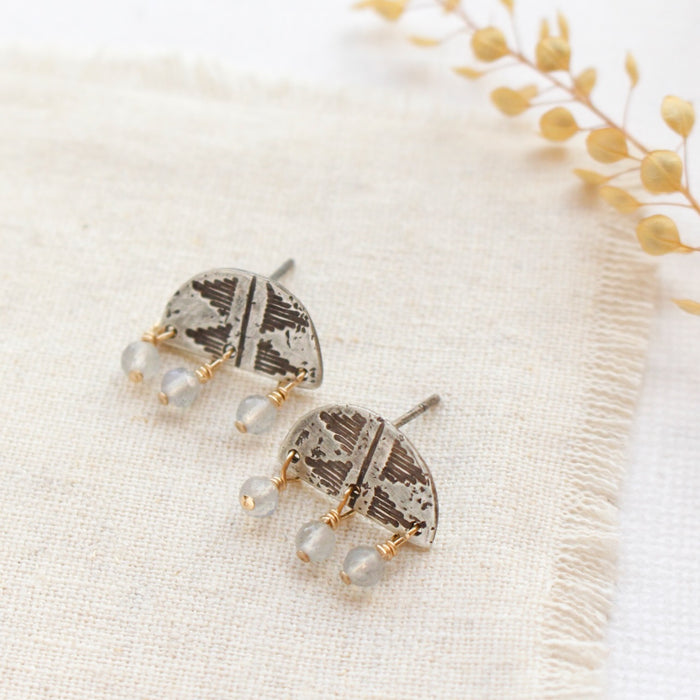 The labradorite pakal arch earrings styled on linen with dried grass