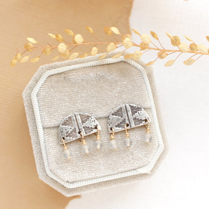 The labradorite mixed metal pakal arch post earrings styled on a velvet box with dried grass