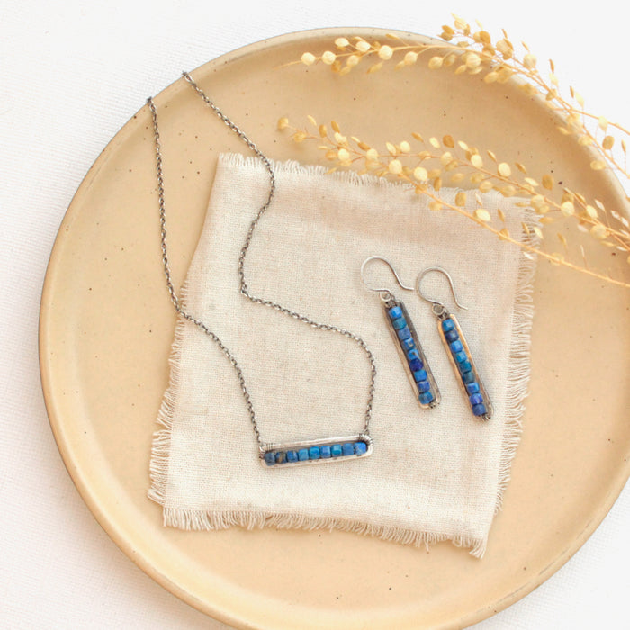 The lapis beaded bar necklace styled with the matching earrings on a tan plate with linen and dried grass