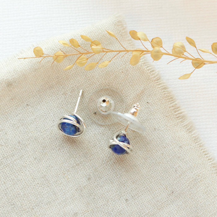 The lapis wrapped post earrings styled on linen with dried grass