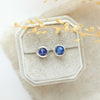 The silver wrapped lapis post earrings styled on a velvet box with linen and dried grass