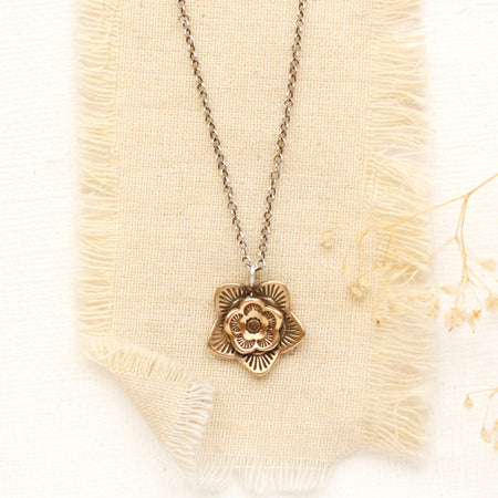 The bronze layered cactus flower necklace styled on tan linen with dried grass