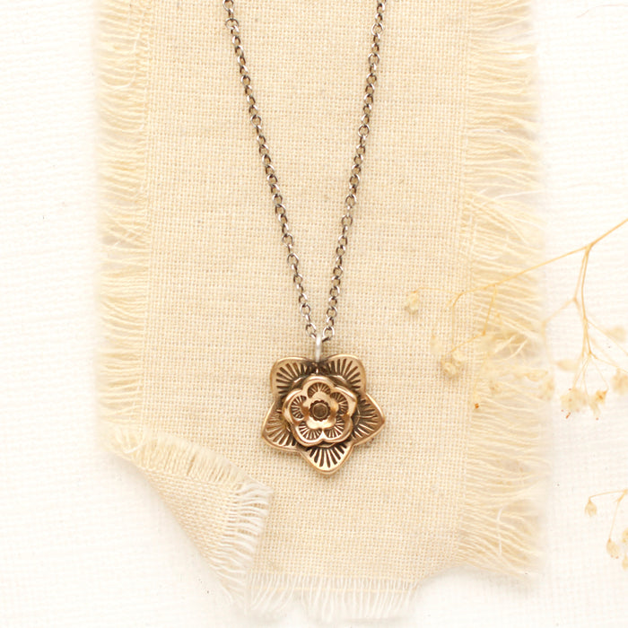 The bronze layered cactus flower necklace styled on tan linen with dried grass