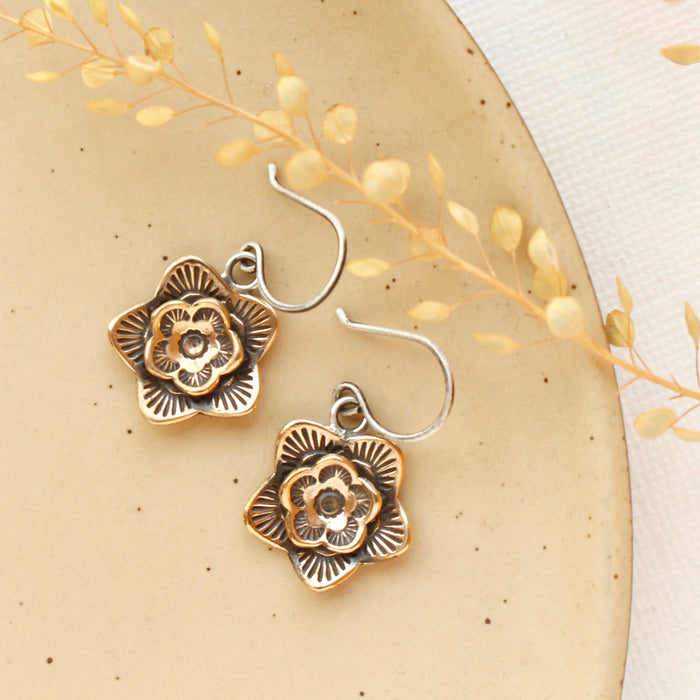 The bronze layered cactus flower earrings styled on a tan plate with dried grass