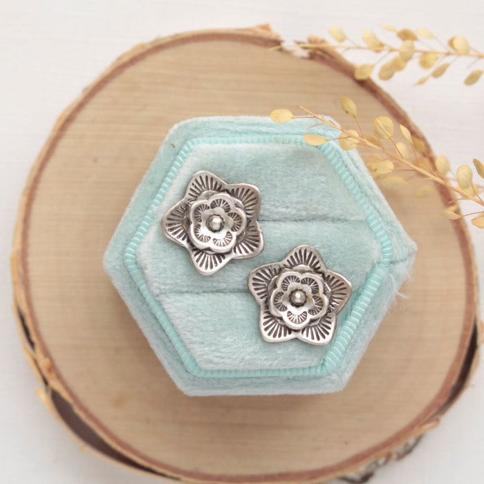 The layered cactus flower post earrings styled on a blue velvet box with wood and dried grass