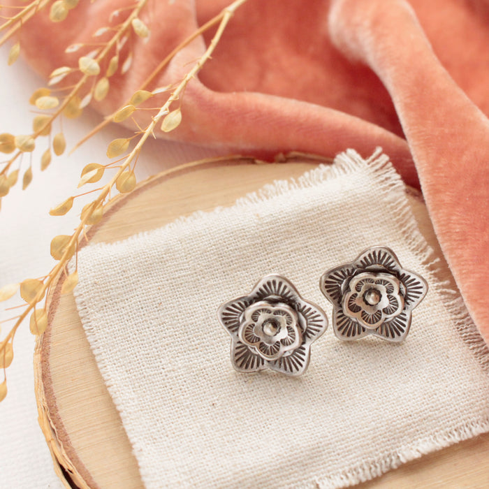 The layered cactus flower post earrings styled on wood with linen, orange velvet, and dried grass