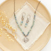 The layered talara knotted kyanite necklace styled with the matching earrings on a tan plate with linen and dried grass