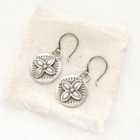 The layered wanderer coin earrings styled on tan linen