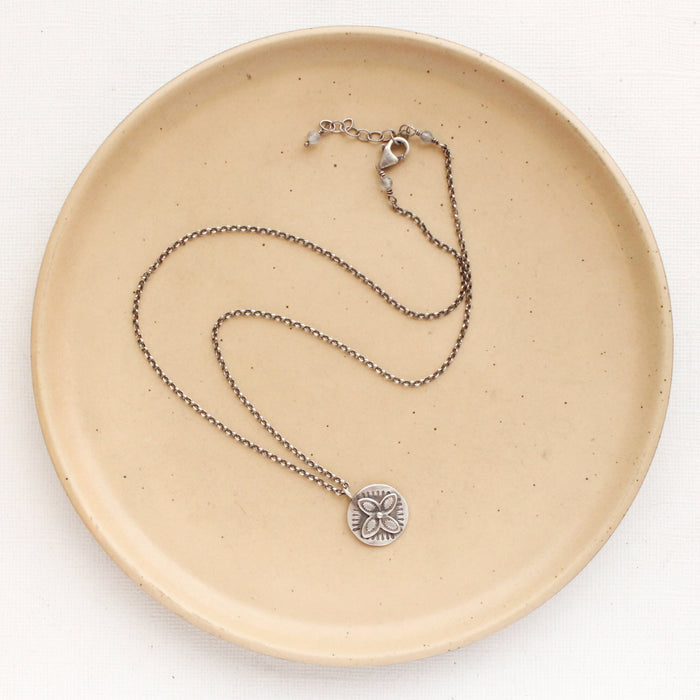 The layered wanderer coin necklace styled on a tan plate to show the adjustable lobster clasp closure