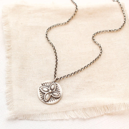 The layered wanderer coin necklace styled on tan linen